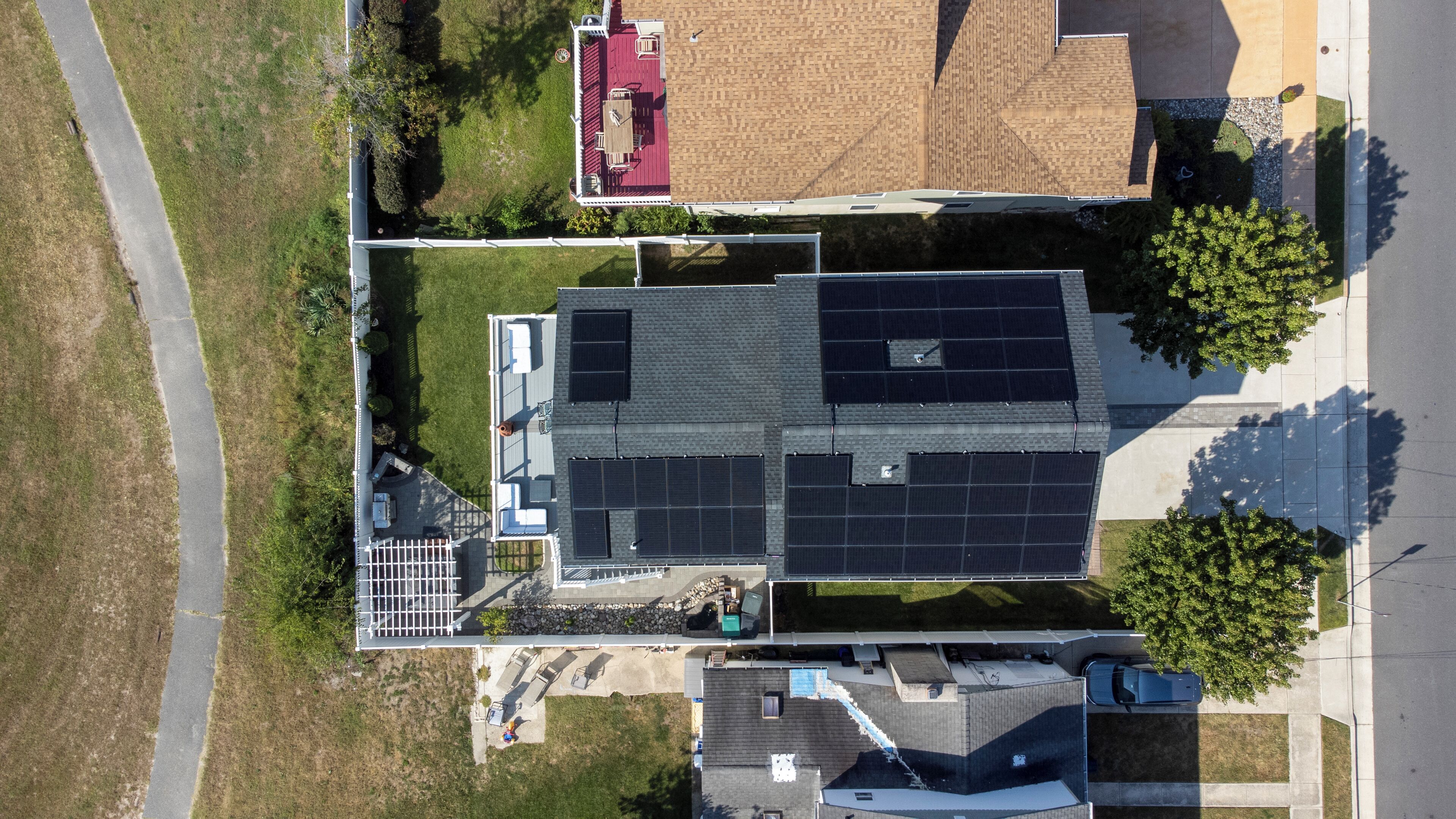 Vista aérea de una zona residencial con una casa que tiene paneles solares, techo rojo y patio cercado.