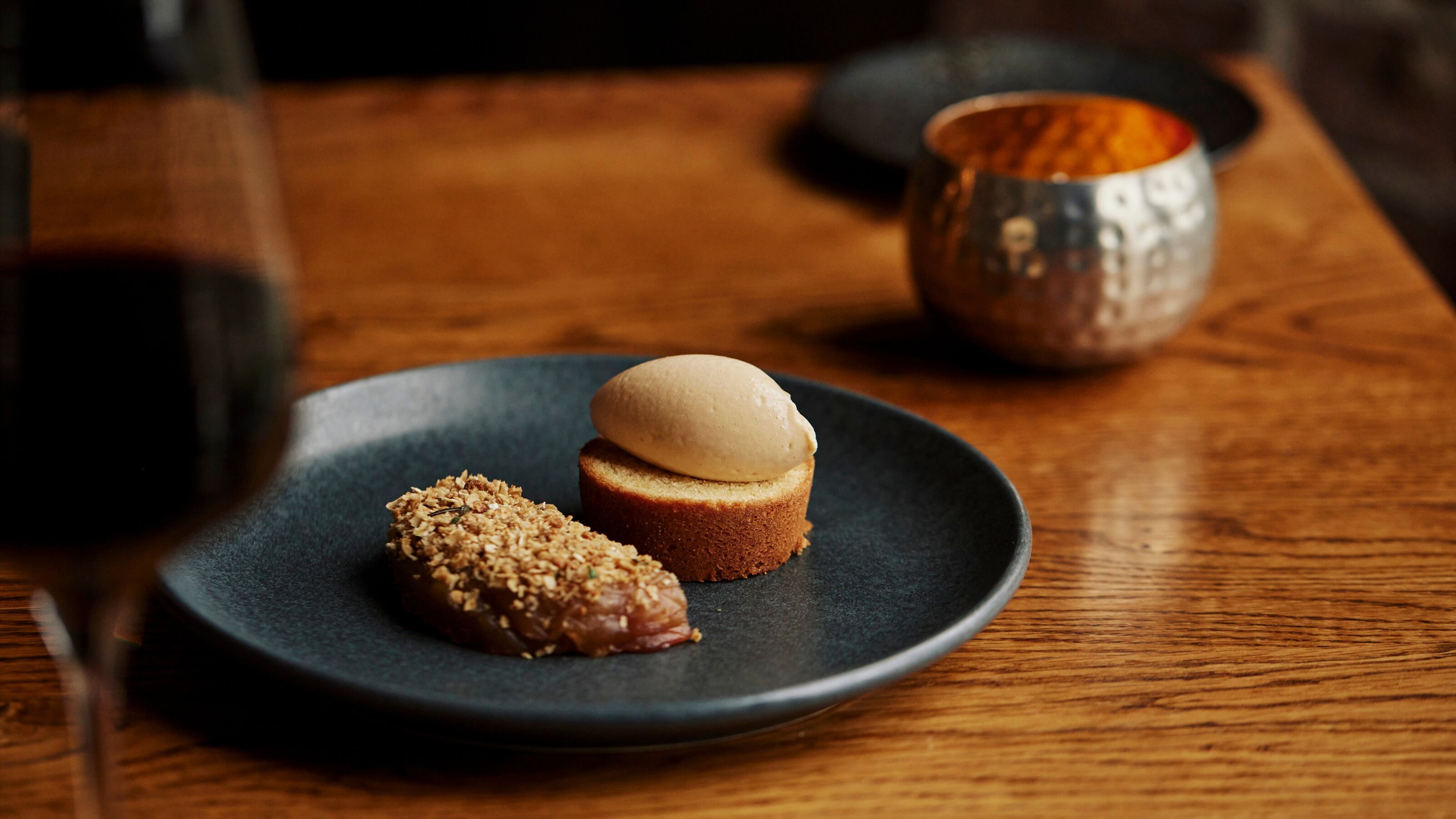 Un plato de postre con pastel y una bola de helado sobre un plato oscuro.