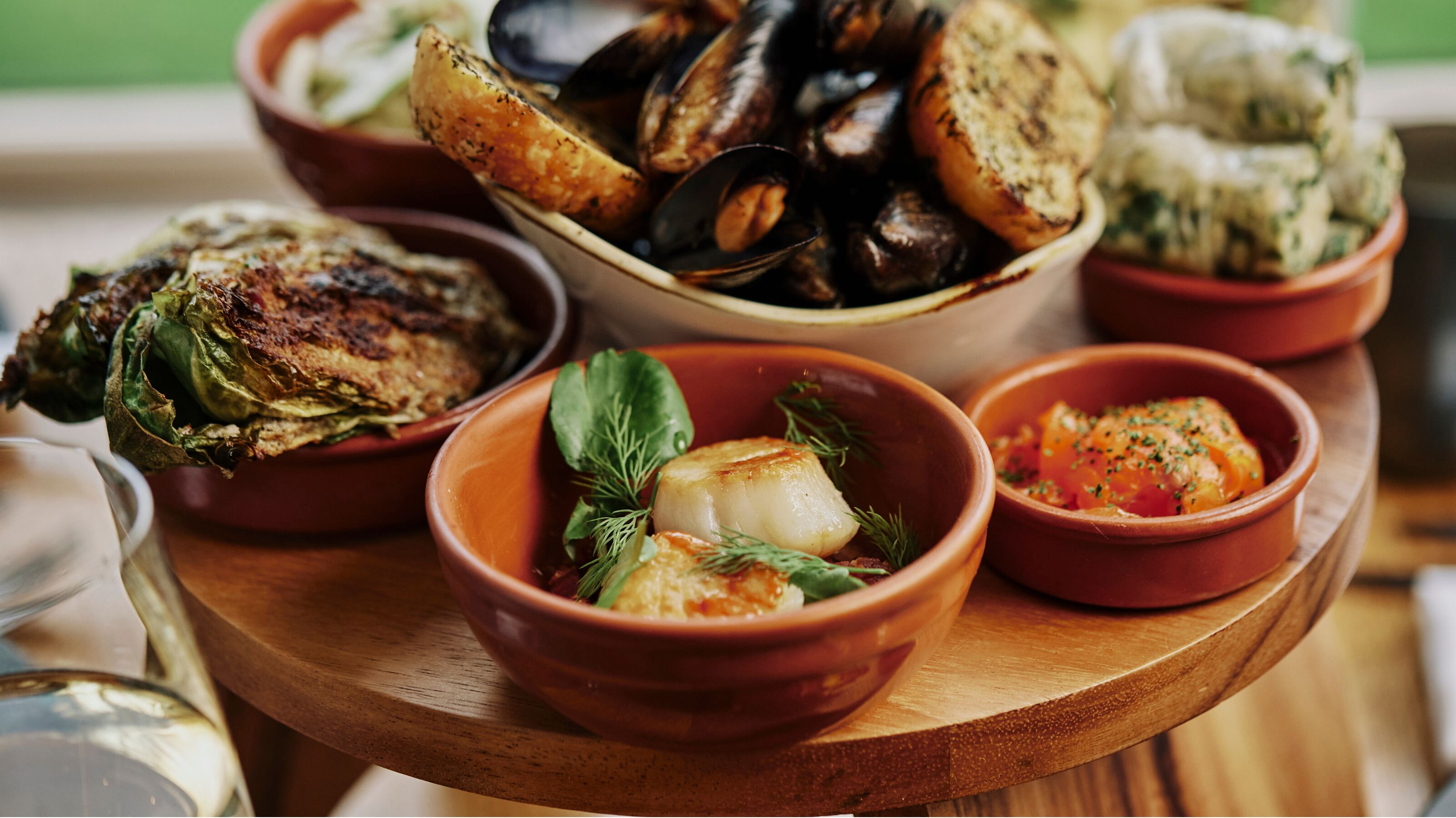 Una mesa de madera con diversos platos, incluyendo mejillones, pescado a la parrilla y verduras.