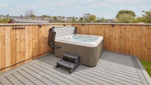 Un jacuzzi en una terraza de madera, con un cerco de madera al fondo.