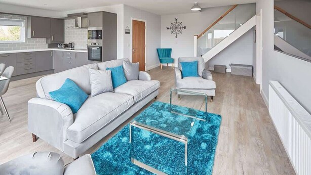 Una sala de estar moderna con un sofá gris, un sillón azul y una mesa de centro de vidrio.