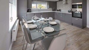 Una cocina moderna con armarios grises, horno integrado y comedor con mesa y sillas de vidrio.