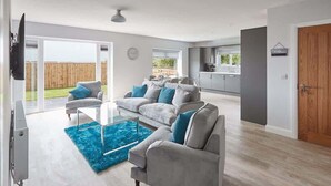 Una sala de estar moderna con sofás grises, un tapete azul y una cocina al fondo.