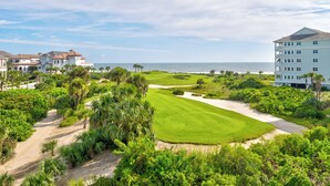 A golf course with a view of the ocean, surrounded by lush greenery and a large building. - Renovated - 4th Floor Condo #143 with Golf & Ocean Views at Cinnamon Beach (Palm Coast)