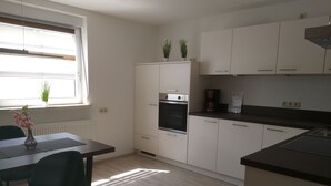 A modern kitchen with white cabinets, a built-in oven, and a dining area with a table and chairs.