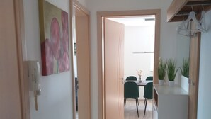 A hallway with a wooden floor, a painting on the wall, and a door leading to a dining area with chairs and a table.