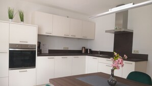 A modern kitchen with white cabinets, a built-in oven, a dark countertop, and a vase with flowers on the dining table.