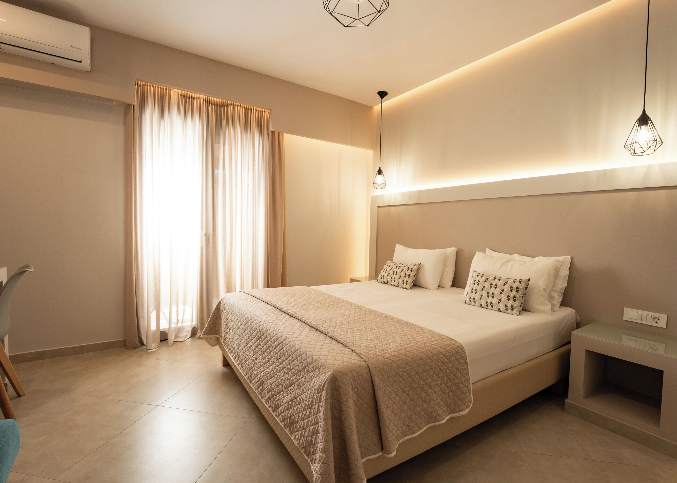 A modern hotel room with a large bed, a bedside table, a nightstand, a lamp, and an air conditioning unit.