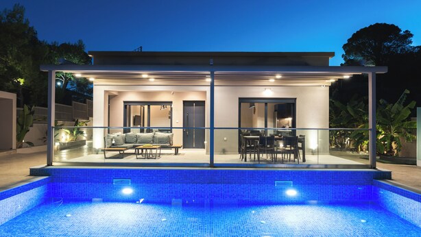 A modern house with a glass-enclosed patio, a pool, and a dining area. - Amelia Residence (Zakynthos)