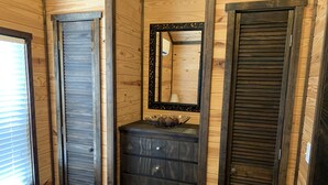 Une pièce aux murs en bois, avec une commode à tiroirs, un miroir et une fenêtre équipée de stores.