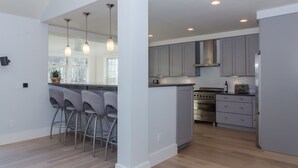 A modern kitchen with grey cabinets, a central island with bar stools, stainless steel appliances, and pendant lighting. - Costal Country Summer Home with Beach Access - 3 building compound (Westport)