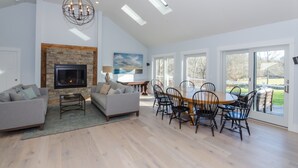 A spacious living room with a fireplace, a dining area with a wooden table and chairs, and large windows offering a view of the outdoors. - Costal Country Summer Home with Beach Access - 3 building compound (Westport)