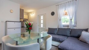 A modern living room with a glass-top dining table, a grey sofa, and a kitchen area in the background. - Nina in Peroj  - Haus für 6 Personen (Fazana)
