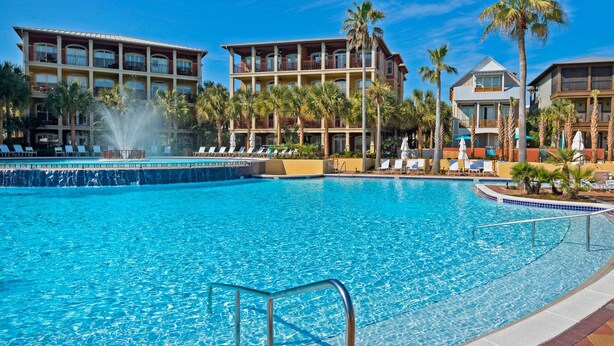 A large outdoor swimming pool with a fountain, surrounded by palm trees and lounge chairs.