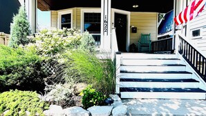 A house with a covered porch, a stone wall, and a flag. - Lakewood's Cozy Cottage ~~all inquiries welcome!~~ (Lakewood)