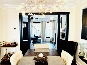 Ett modernt vardagsrum med en matplats, med ett träbord, två vita stolar med vaddering, en dekorativ mittendekoration och en unik taklampa.