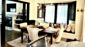 A dining area with a wooden table, white upholstered chairs, and a chandelier. - Lakewood's Cozy Cottage ~~all inquiries welcome!~~ (Lakewood)