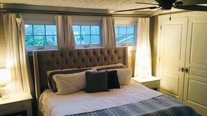 A bedroom with a tufted headboard, a large window with curtains, a ceiling fan, and a wardrobe. - Lakewood's Cozy Cottage ~~all inquiries welcome!~~ (Lakewood)