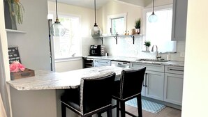 A modern kitchen with a marble countertop, black bar stools, pendant lights, and a coffee machine. - Lakewood's Cozy Cottage ~~all inquiries welcome!~~ (Lakewood)