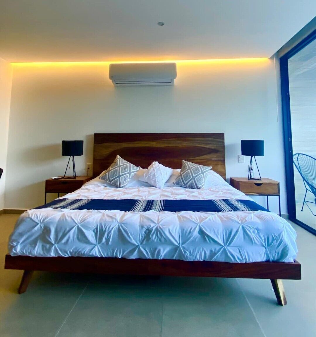 Une chambre moderne avec un grand lit, deux tables de chevet et une vue sur la mer par une grande fenêtre.