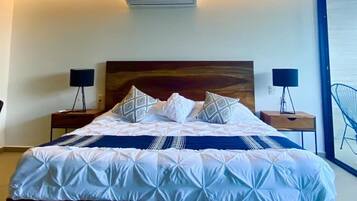 A modern bedroom with a large bed, two bedside tables, and a view of the sea through a large window.