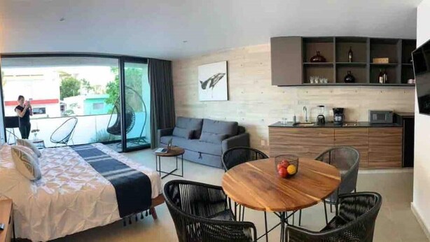 Een moderne hotelkamer met een bed, een bank, een eettafel en een keukenhoek.