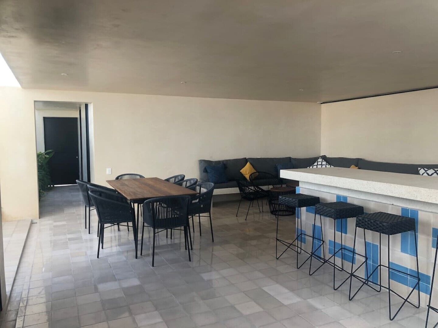 Une cuisine moderne avec un coin repas, comprenant une table et des chaises en bois, un comptoir-bar avec des tabourets et un canapé avec des coussins.