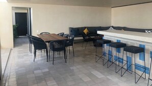 Een moderne keuken met een eethoek, met een houten tafel en stoelen, een bargedeelte met krukken, en een bank met kussens.