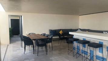 A modern kitchen with a dining area, featuring a wooden table and chairs, a bar counter with stools, and a sofa with cushions.