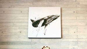 Een moderne woonkamer met een ronde houten salontafel, een donkere vaas met gedroogde bloemen en een grijze bank. Daarboven hangt een groot abstract schilderij aan de muur.