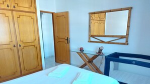 A room with a bed, wooden wardrobe, a mirror, and a small table with a globe and statue.