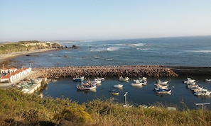 A coastal marina with boats docked, a rocky breakwater, and buildings with red roofs.