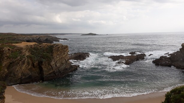 A coastal landscape with rocky cliffs and a sandy beach.