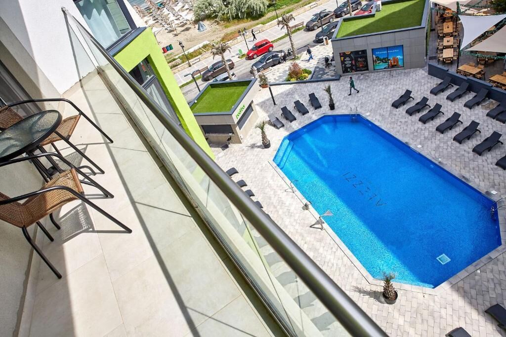 A rooftop pool with lounge chairs, a table, and a view of the street below.