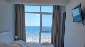 Een hotelkamer met een groot bed, een televisie aan de muur en uitzicht op zee.