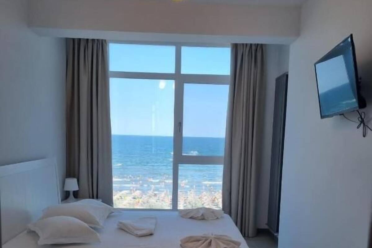 Une chambre d’hôtel avec un grand lit, un téléviseur fixé au mur et une vue sur la mer.