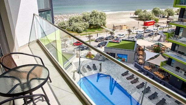 Een balkon met glazen hekwerk met uitzicht op een strand, een zwembad en een restaurantgedeelte.