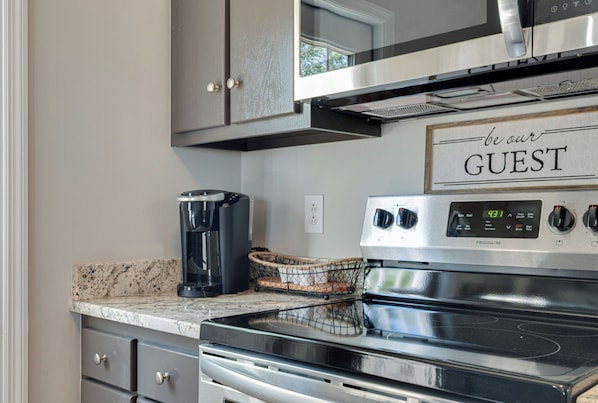 A kitchen with a stainless steel stove, a coffee maker, and a sign that says "be our GUEST".