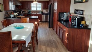 Cucina con mobili in legno, un tavolo da pranzo con sedie, un frigorifero e una macchina per il caffè.