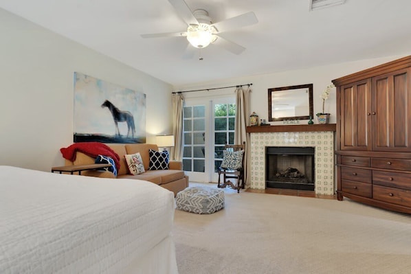 A bedroom with a bed, a ceiling fan, a fireplace, and a large wooden cabinet.