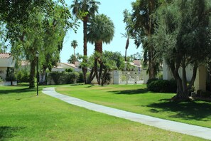 A well-maintained grassy area with a curved pathway, surrounded by various trees and a white fence.