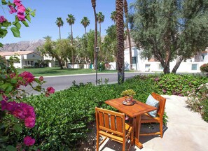 A wooden table and chair set outdoors with a view of a street and houses in the background. - La Hacienda | 3BR Santa Rosa Cove (La Quinta)