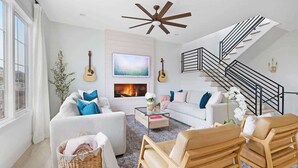 A modern living room with a fireplace, a staircase, and a large window. - The Jolene – Rooftop w/ Firepit, Close to 12 South (Nashville)