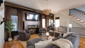 A modern living room with a fireplace, comfortable seating, a television, and a staircase. - The Gambler - Pool Table + Rooftop Lounge! (Nashville)