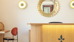 Una recepción con mostrador de madera, un espejo redondo con marco dorado y dos luces fijadas a la pared.