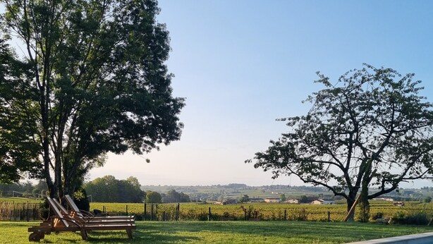 Una piscina con zona verde y árboles, un banco y vistas a campos lejanos.