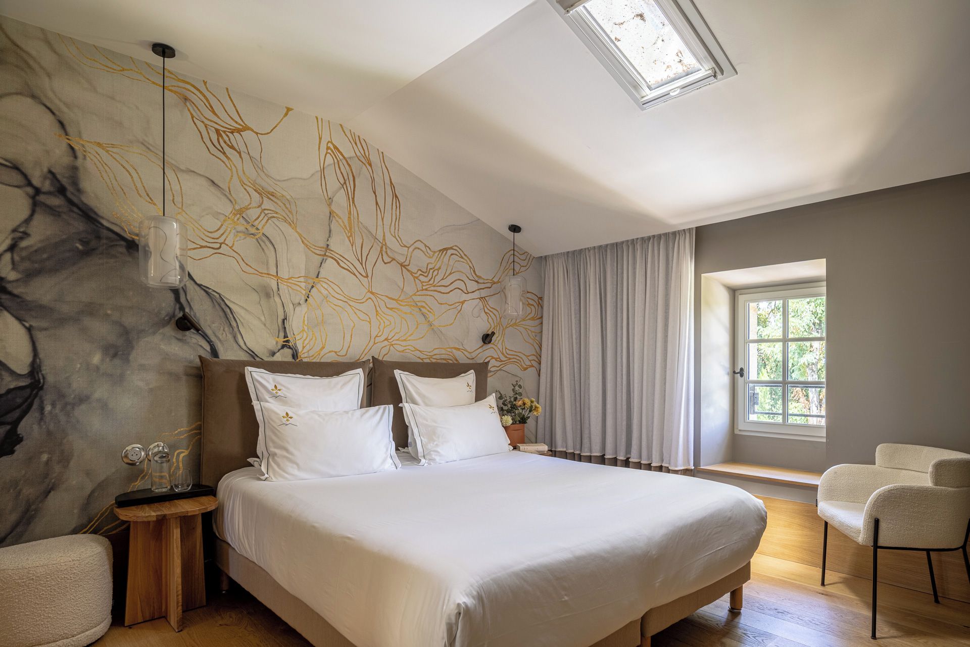 Ein modernes Schlafzimmer mit einem großen Bett, einer Marmorwand, einem Oberlicht und Blick auf Grün durch ein Fenster.