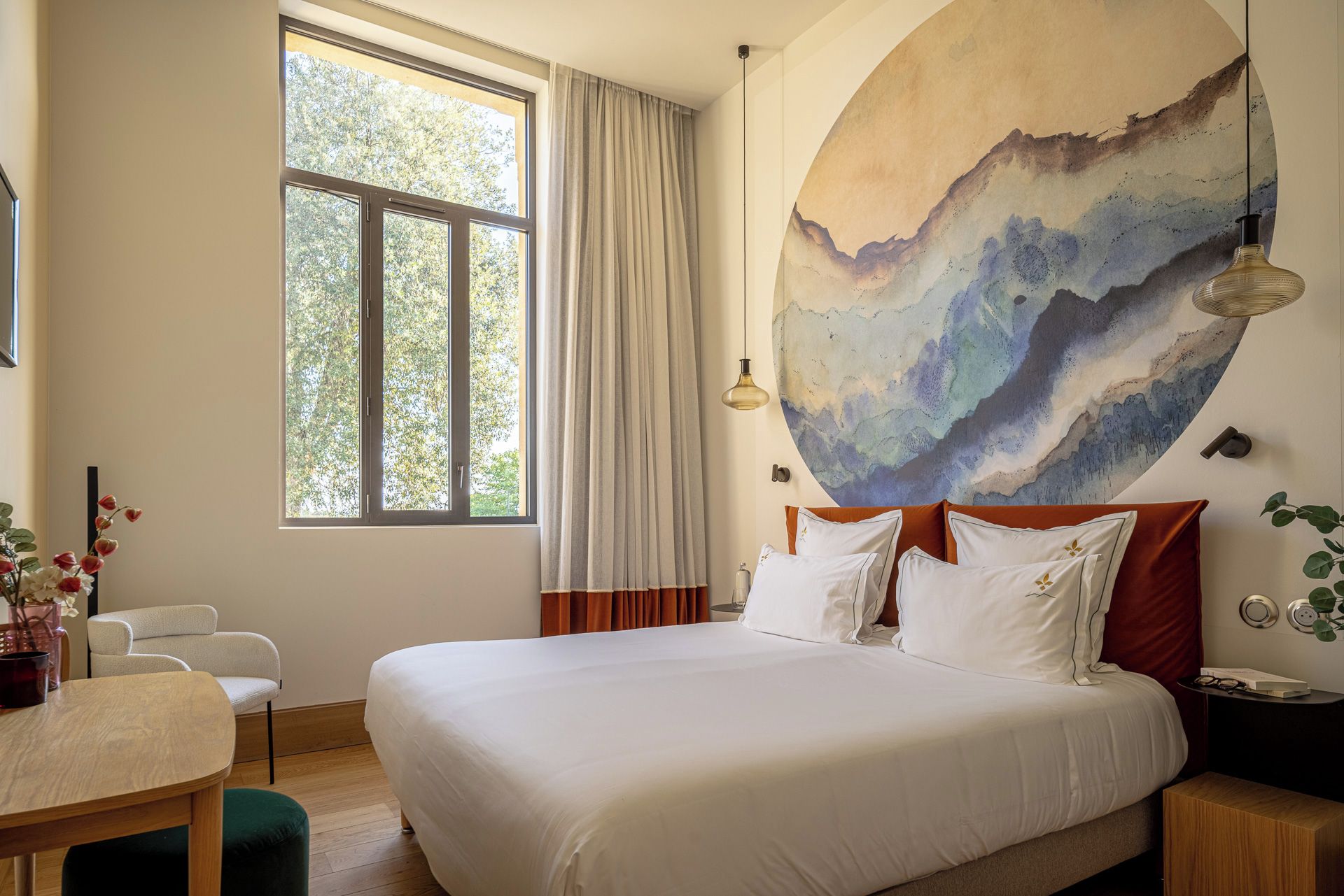 Une chambre d’hôtel avec un grand lit, un bureau, une chaise, une fenêtre avec des rideaux et un tableau au mur.