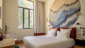 Une chambre d’hôtel avec un grand lit, un bureau, une chaise, une fenêtre avec des rideaux et un tableau au mur.