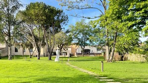 Un patio arbolado con césped y senderos de piedra, edificios de fachada de piedra y estuco.